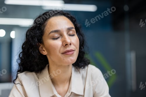Preview: Relaxed hispanic businesswoman with closed eyes enjoying a moment of peace during busy office day