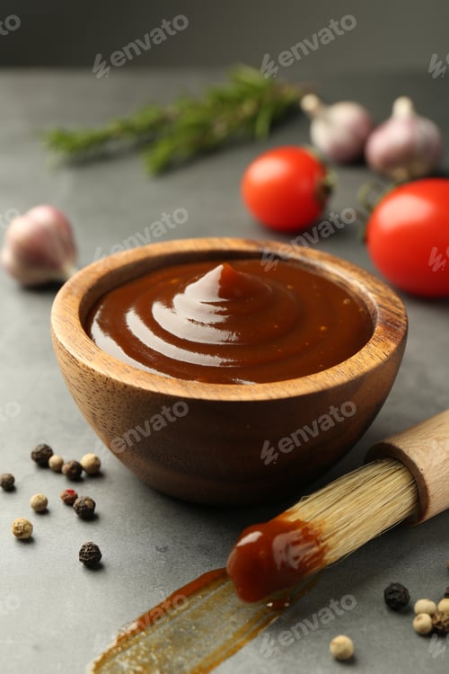 Preview: Tasty barbeque sauce in bowl, brush and peppercorns on grey table, closeup
