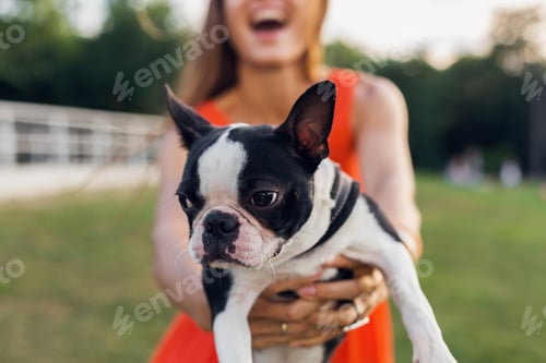 Preview: young happy smiling woman in orange dress having fun playing with dog in park