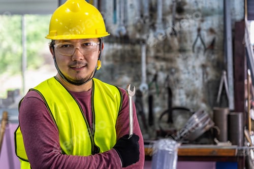 Preview: Portrait of Asian machinist in safety suit holding the wrench over the stack of wrench