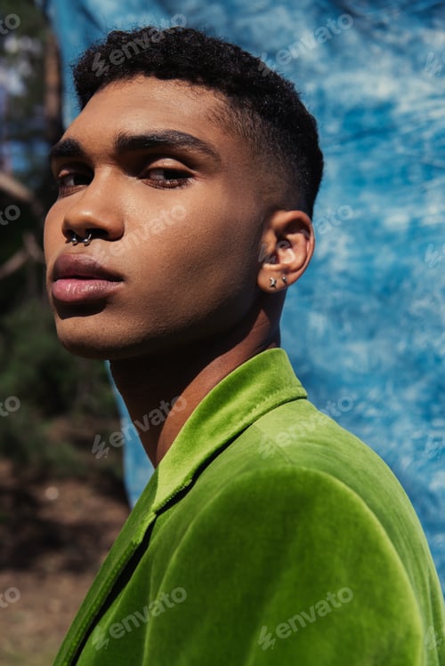 Preview: portrait of african american man with piercing looking at camera near blue cloth on blurred