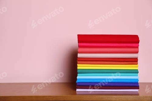 Preview: Pile of bright t-shirts on table against color background