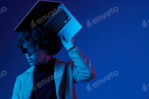 Preview: Portrait of a stylish male hacker with a laptop and futuristic glasses in blue light, cyber security