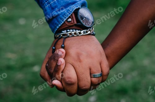 Preview: father holding the hand of his son both of brown skin, with bracelets and watch