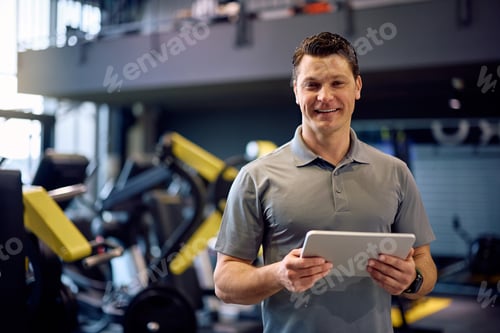 Preview: Happy personal coach with touchpad in a gym looking at camera.