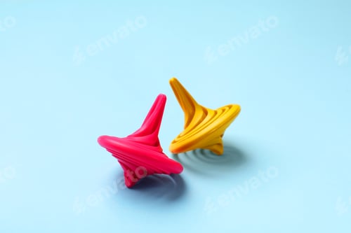 Preview: Yellow and pink spinning tops on light blue background, closeup