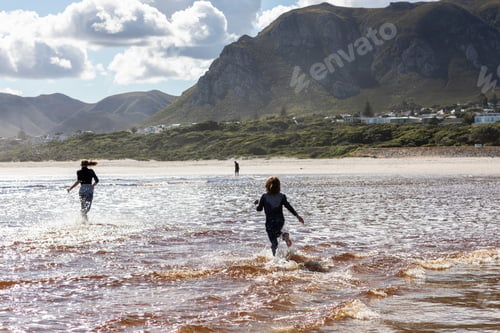 Preview: Teenage girl and a boy running through shallow water on a wide sandy beach