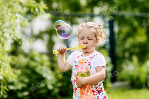 Preview: A little girl blows soap bubbles in the park. Happy childhood, summer time. Side view