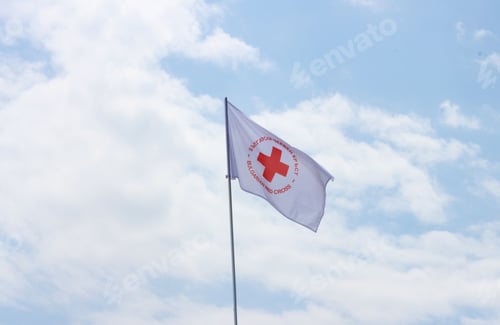 Preview: White flag withe red cross, medical center flag against the sky