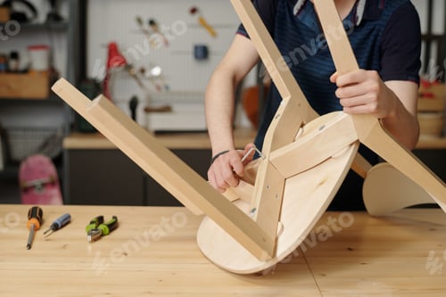 Preview: Hands of teenage guy with handtool fixing back of wooden chair seat