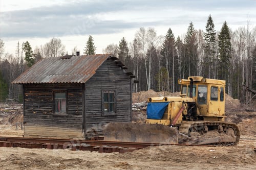 Preview: Yellow bulldozer in the sand near the wooden house