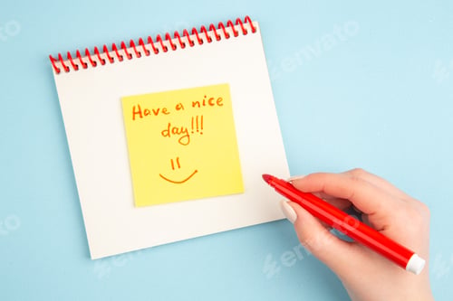 Preview: top view spiral notebook female hand writing have a nice day on yellow sticky note on blue