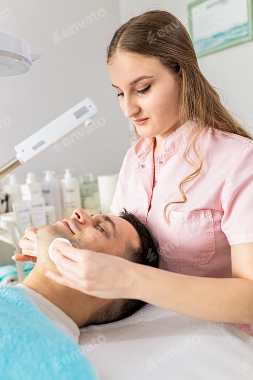 Preview: Beautician doing face treatment in beauty salon to a male customer.