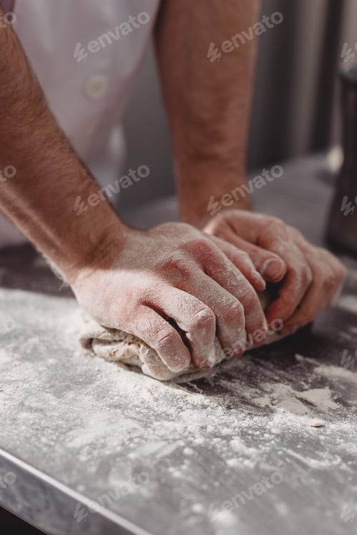 Preview: Professional baker kneads dough on the table in the kitchen of the bakery