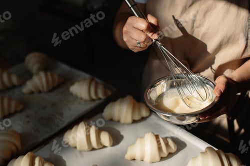 Preview: Female baker smears raw croissants with a brush in the yolk, the cooking process.