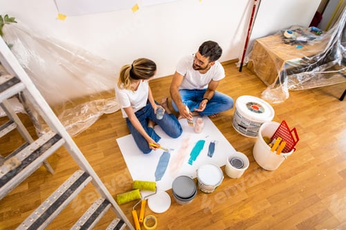 Preview: Young couple sitting on the floor choosing color for painting the wall in their home.