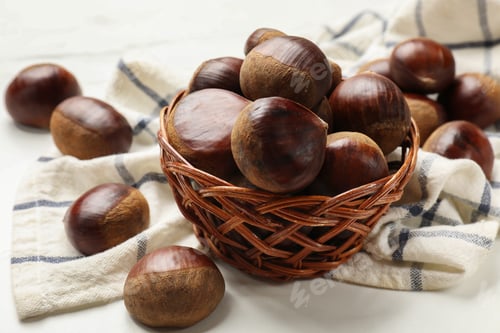 Preview: Sweet fresh edible chestnuts in wicker bowl on white table, closeup