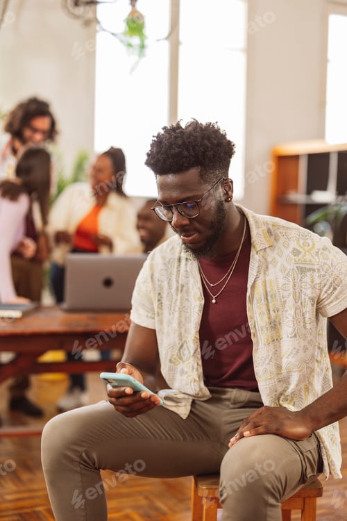 Preview: african man using smart phone in modern office, colleagues in background