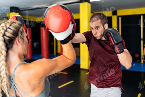 Preview: Young kickboxer male practicing punching with his female colleague wearing mittens