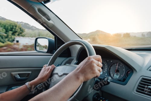 Preview: Hands of woman driving a car at sunset with sunlight on background