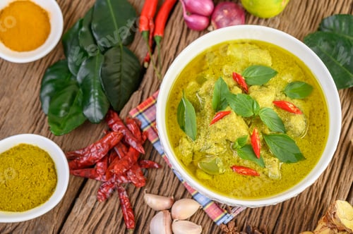 Preview: Green curry in a bowl and spices on wooden table.