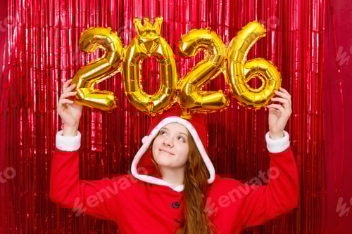 Preview: Cute girl in a santa costume holding golden balloons with the shape 2026