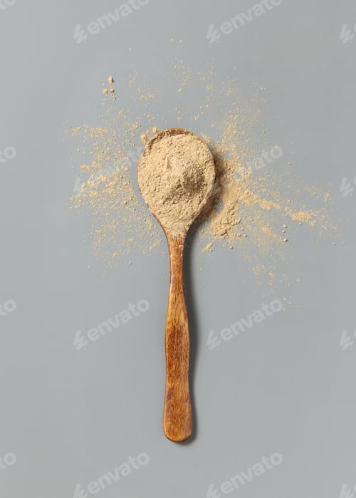 Preview: Wooden spoon full of beige powder on grey top view. Dietary supplement or kitchen spice