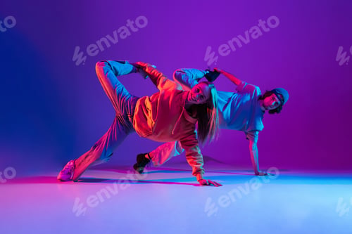 Preview: Young man and woman dancing hip-hop in casual sports youth clothes on gradient purple pink