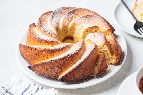 Preview: Vanilla biscuit cake with powdered sugar on white plate on light gray background.