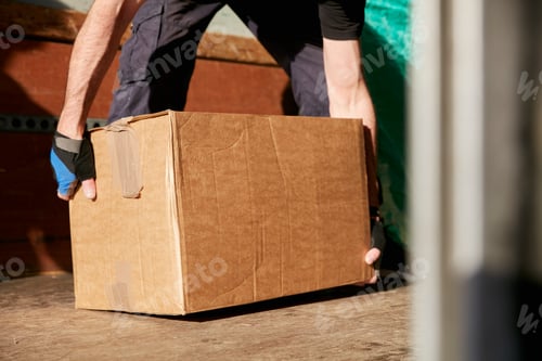 Preview: Removals business. A man lifting a cardboard box off the floor.