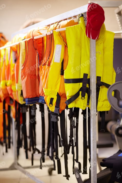 Preview: Ready when needed. Cropped shot of life jackets hanging on a rail inside a lifeguard station.