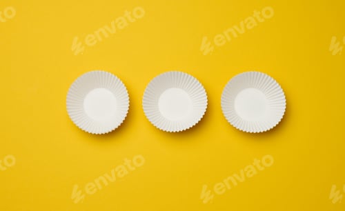 Preview: Empty white paper cupcake molds on yellow background, top view