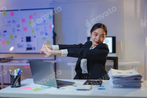 Preview: Asian businesswoman stretching arms during late-night office work, relaxing at desk