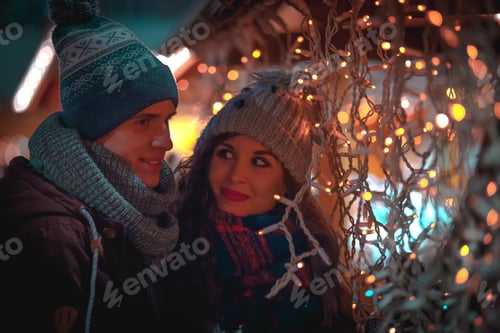 Preview: Couple in warm clothes enjoying colorul Christmas market, bokeh lights background