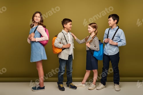 Preview: Full length of smiling interracial kids with backpacks looking at friends talking during