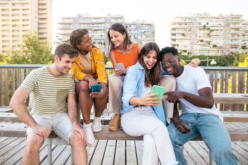 Preview: Group of young people standing together while sitting in wooden bench in the city - Funny