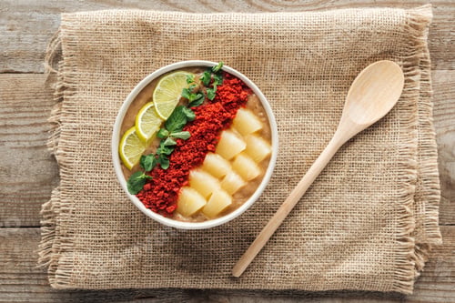 Preview: top view of fresh smoothie bowl with lemons, mint and pineapples on sackcloth