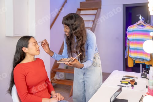 Preview: Makeup artist applying makeup to woman's face in front of a mirror. People together having fun.