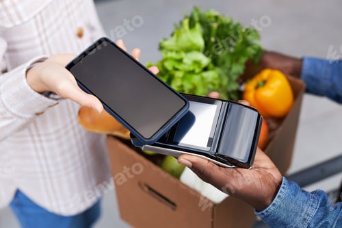 Preview: Top view closeup of woman paying for grocery delivery via smartphone NFC
