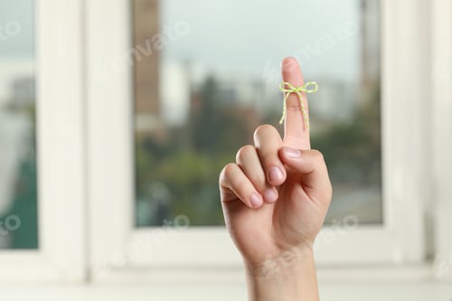 Preview: Man showing index finger with tied bow as reminder near windows indoors, closeup. Space for text