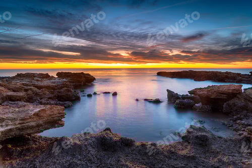 Preview: Beautiful sunrise over rocks at the beach at Torre de la Sal