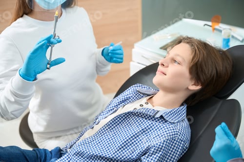 Preview: Smiling teenager looking at syringe with anesthesia in hands dentist