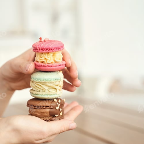 Preview: Close-up of diverse macarons in hands with pastel colors and creamy fillings