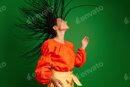 Preview: Attractive young woman with dreadlocs dancing and looking joyful against green background
