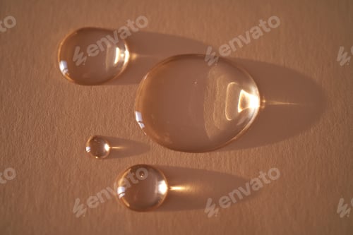 Preview: Beautiful volumetric drops of cosmetic product on a beige background.