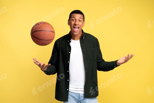 Preview: Happy sportsman throwing up basketball ball standing over isolated yellow background
