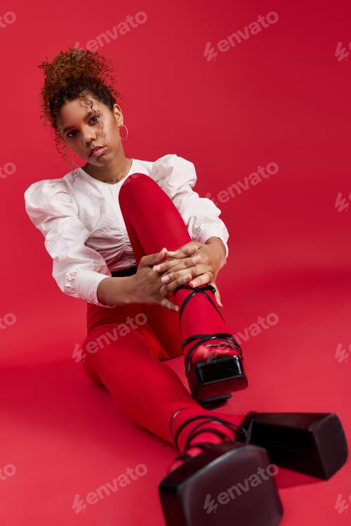 Preview: Stunning woman in vibrant fashion against a bold red backdrop in a creative studio