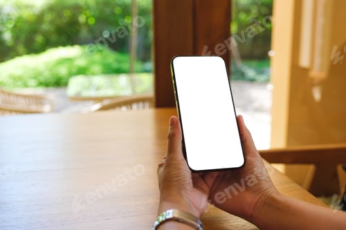 Preview: Mockup image of a woman holding and using mobile phone with blank desktop at home