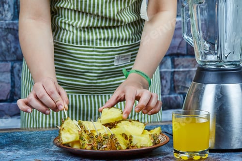 Preview: Hand holding slices of pineapple next to teapot and a glass of juice on blue background