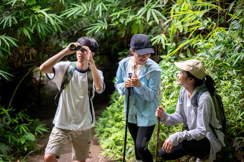 Preview: A man looking through binocular standing with woman friends resting during forest hiking or trekking